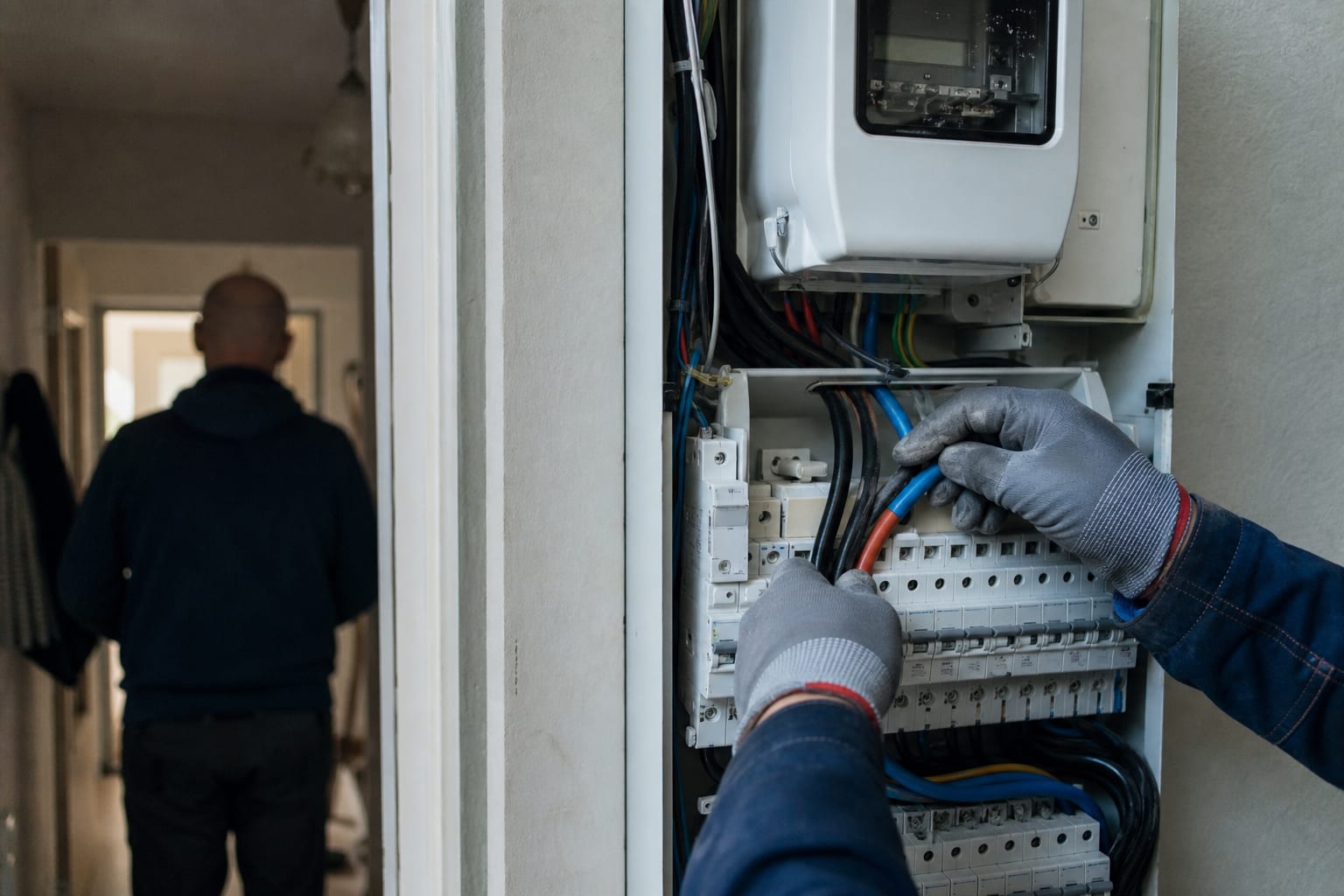 Électricien intervenant sur un tableau triphasé dans l'entrée d'une maison.