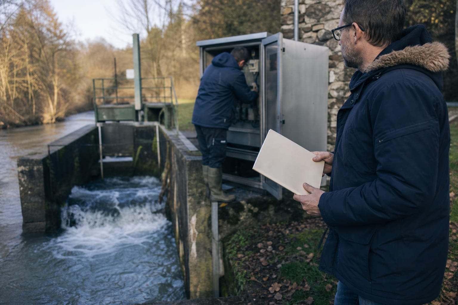 Ouvrier contrôle une petite centrale hydroélectrique et un certificat plié.