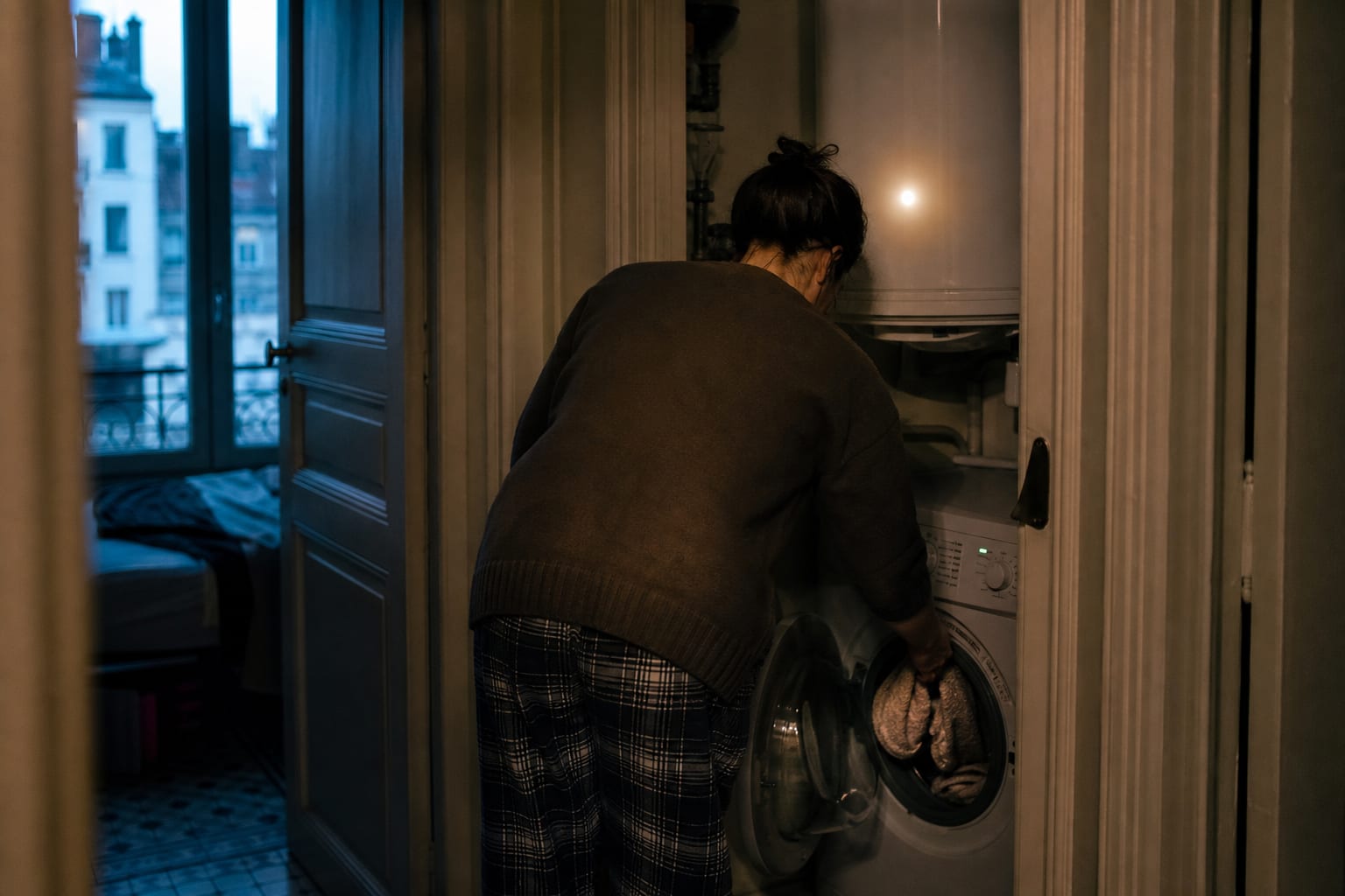 Habitante chargeant son lave-linge le soir dans un appartement lyonnais.