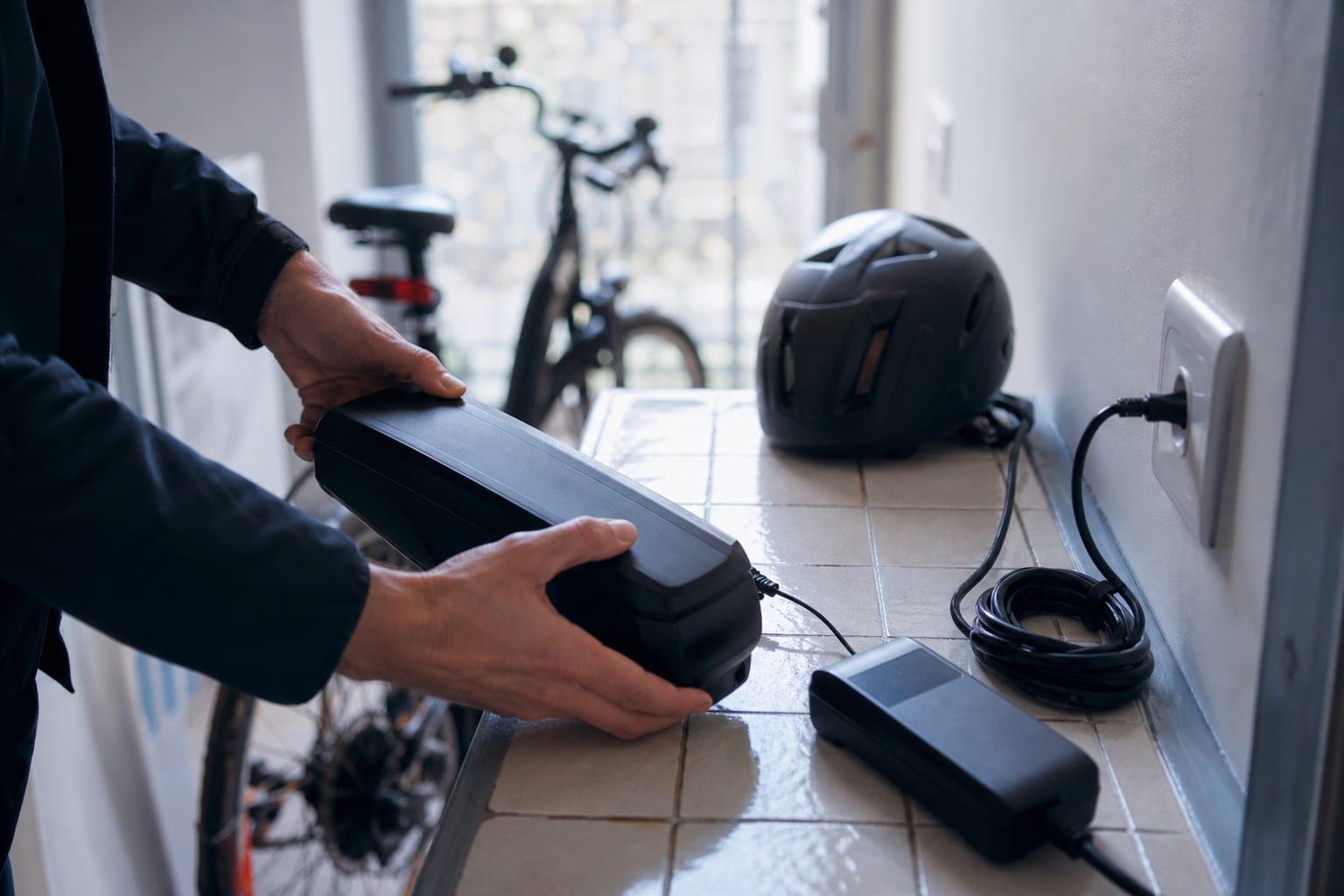 Mains rechargeant une batterie de vélo près d’une prise domestique.